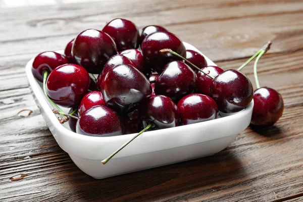 Frische reife, saftige Süßkirschen in einem weißen Teller auf einem hölzernen Hintergrund. — Stockfoto