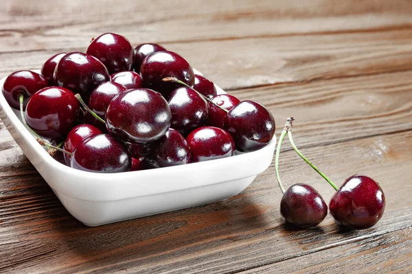 Rote frische reife, saftige Süßkirschen in einem weißen Teller auf einem hölzernen Hintergrund. — Stockfoto