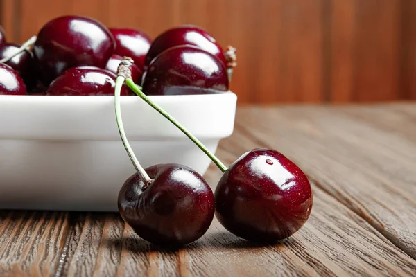 Rote frische reife, saftige Süßkirschen auf einem weißen Teller und zwei Früchte auf einem hölzernen Hintergrund. — Stockfoto