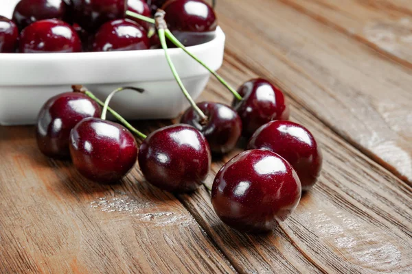 Frische reife, saftige Süßkirschen auf einem weißen Teller und auf einem hölzernen Hintergrund. Nasse Kirschen mit Spritzern und Wassertropfen. . — Stockfoto