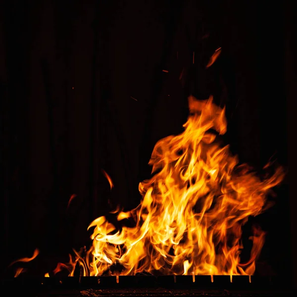 Llama de fuego brillante sobre un fondo oscuro. Fuego ardiente por la noche. Un fuego en la parrilla, chimenea y hogar . —  Fotos de Stock