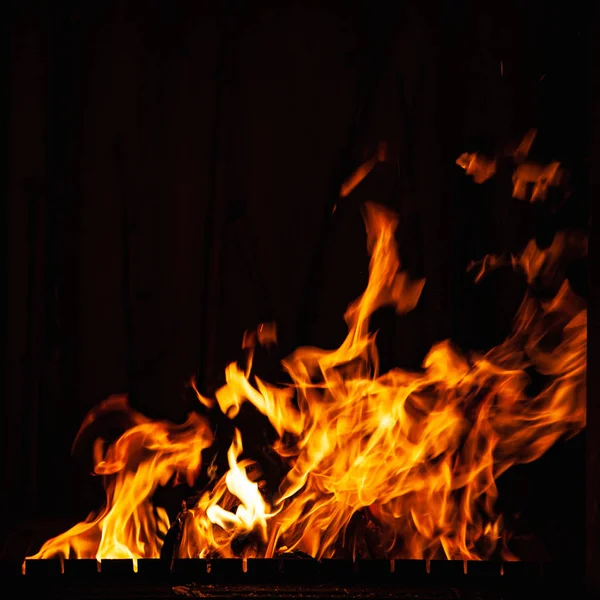 Llama de fuego sobre un fondo oscuro. Fuego ardiente por la noche. Un fuego en la parrilla, chimenea y hogar . —  Fotos de Stock