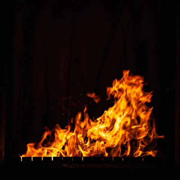 Llama de fuego sobre un fondo oscuro. Luminoso fuego ardiente por la noche. Un fuego en la parrilla, chimenea y hogar . —  Fotos de Stock