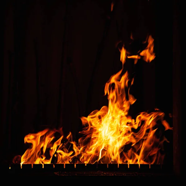 Llama de fuego sobre un fondo oscuro. Fuego ardiente por la noche. Luminosa hoguera en la barbacoa, chimenea y hogar . —  Fotos de Stock