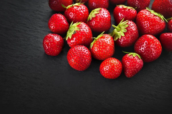 Bir yığın çilek arka planı. Koyu bir taşın üzerinde çilek. Kopya alanı olan arkaplan resmi. Sağlıklı meyveler. Doğal organik gıda..