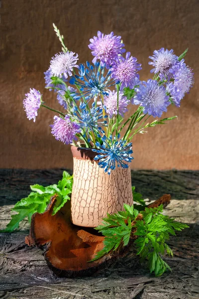 Bouquet of clover and garlic flowers in a vase. Rustic still life with clover wildflowers and tree bark. Selective soft focus. Natural still life.