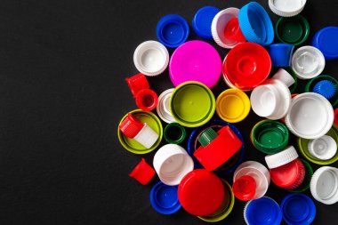 Siyah arka planda fotokopi alanı olan bir yığın plastik şişe kapağı. Geri dönüştürülmüş plastik şişe kapakları. Ayrı çöp toplama yeri. Protez için plastik geri dönüşümü. Seçici odaklanma. Çok renkli desen.
