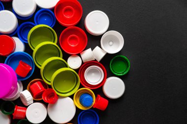 Siyah arkaplanda fotokopi alanı olan renkli PET kapaklarının üst görünümü. Geri dönüştürülmüş plastik şişe kapakları. Ayrı çöp toplama yeri. Protez için plastik geri dönüşümü. Seçici odaklanma. Çok renkli desen.