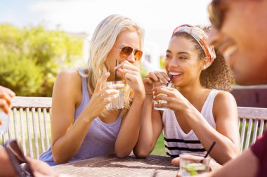 Genç kadınlar Açık ve içme limon suyu dedikodu. Gülüyor ve açık kafede oturan neşeli çok ırklı kızlar. Arkadaşlar yaz tatili birlikte eğleniyor.