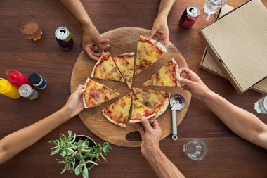 Üstten görünüm Grubu'nun İtalyan pizza paylaşımı eller. Arkadaşlar el restoranda pizza dilimleri ahşap kesme tahtasından alarak yüksek açılı görünüş. Evde pizza bir üçgen alan çok ırklı insanlar.
