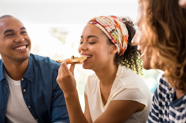 非洲女人坐在一起吃披萨片的画像 朋友们在家里吃披萨派对 男子和年轻女子在午餐休息时一起在家里玩得开心 — 图库照片
