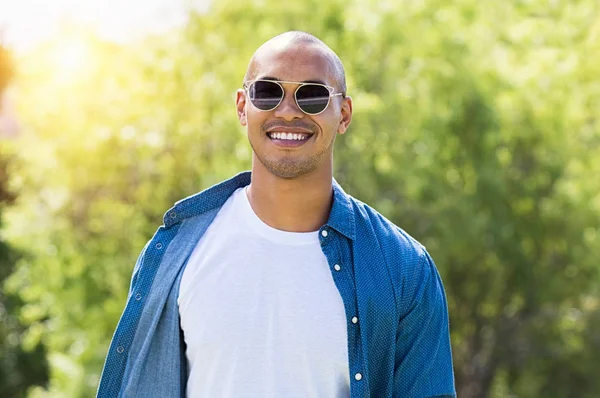 Kameraya bakan güneş gözlüğü ile gülümseyen Afrika adam portresi. Mutlu adam açık yaz zevk. Neşeli genç adam park adlı beyaz tshirt ve mavi tişört giyiyor. 