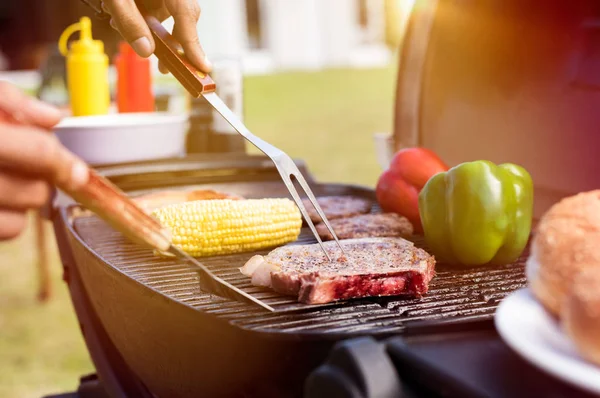 Grilling food at garden party. Closeup of fork being used for baking beef and corn on barbeque with bell peppers. Close up of grilled meat with vegetable over the coals on a bbq.