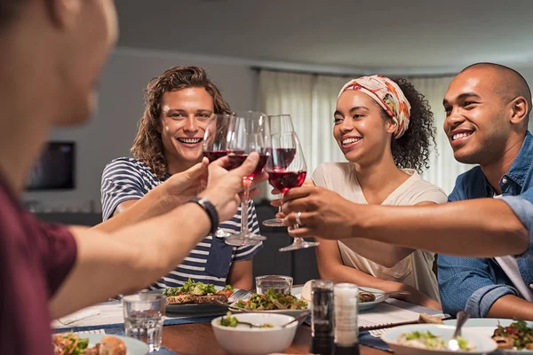 特写的年轻朋友欢呼与红酒 而坐在餐桌上 快乐的美丽的女人和多民族男人在晚宴上举起酒杯 — 图库照片