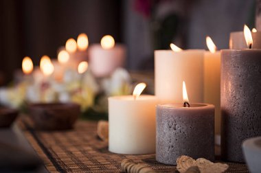 Closeup of burning candles spreading aroma on table in a spa room. Beautiful composition with grey and white candles for spa treatment. Zen and relax concept. clipart
