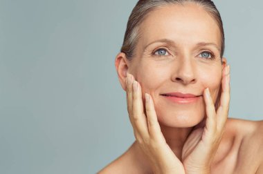 Mükemmel cilt üzerinde gri arka plan izole ile Olgun kadın portresi. Kadın ile kıdemli mutlu portre yüz uzağa arıyorsunuz yanaklarda eller. Kaygısız bir tutum ile karşı karşıya olduğu yaşlanma.