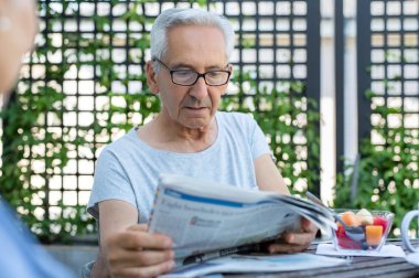 Gazetede bir makale okuma gözlük yaşlı adam. Kahvaltı masasında otururken haber okumak ciddi ifade ile komuta sizde. Olgun adam kötü haber kağıt üzerinde okur.