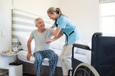 Smiling nurse assisting senior man to get up from bed. Caring nurse supporting patient while getting up from bed and move towards wheelchair at home. Helping elderly disabled man standing up in his bedroom. clipart