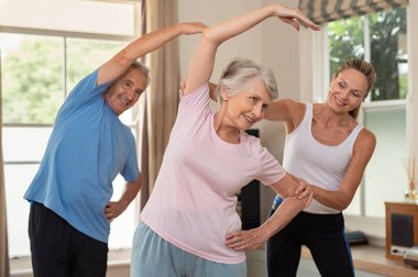 Üst düzey bir çift evde fizyoterapist ile egzersiz yaparak. Yaşlı adam ve yaşlı kadın evde egzersiz yardım olgun spor eğitmeni. Emekli karı koca spor salonunda germe egzersizleri yapıyor.