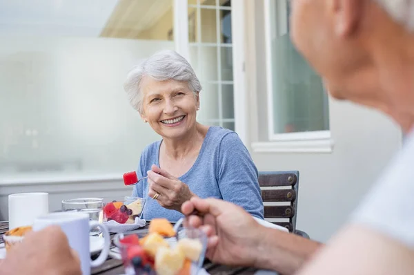 快乐的资深妇女吃新鲜的水果在早餐 开朗的老太太 灰色的头发享受健康的早餐与她的丈夫户外 老夫妇在谈话中享用新鲜水果在阳台上 — 图库照片