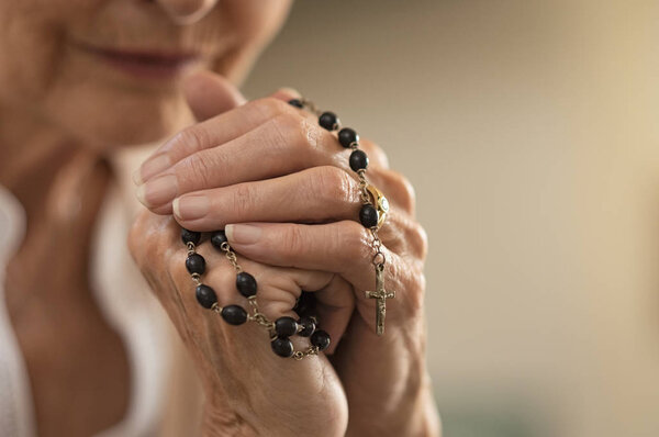 Old wrinkled hands holding a rosary. Closeup of christian senior woman hands holding rosary beads and crucified cross while praying God. Mature catholic lady holding black rosary and praying.
