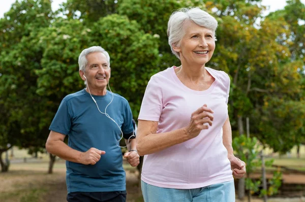 年配のカップルが公園の外で実行されます 老人と老婆のジョギングを一緒に 引退した人間とアクティブな女性の屋外運動 — ストック写真