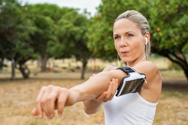 成熟的女人伸展双臂 在听音乐时看着公园 中年跑步者在早上工作 健康运动妇女做伸展运动 — 图库照片