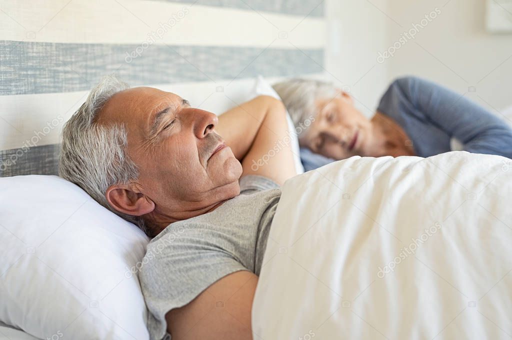 Senior man and woman sleeping on bed. Mature couple resting with eyes closed during the morning. Old husband and wife sleeping together in their bed with peace.