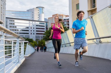 Mutlu bir adam ve güzel kadın birlikte şehir Köprüsü koşu. Sağlıklı iki şehrin sokak üzerinde çalışan. Arka planda bina ile çalışan orta yaşlı çift.