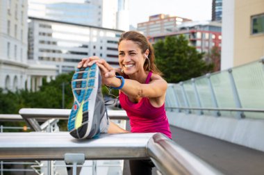 Gülümseyen Olgun kadın bacağı kaldırdı germe yapıyor. Fitness kadın şehirde bacak germe sırasında kulaklık ile müzik dinlemek. Isınma kadar güzel runner.