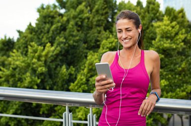 Güzel olgun runner fitness eğitimi dışında sonra dinlenirken cep telefonunda sohbet. Gülümseyen kadın kulaklık müzik dinlerken akıllı telefon ekranına bakarak. Şehirde koşu sonra dinlenme rahat latin kadın.