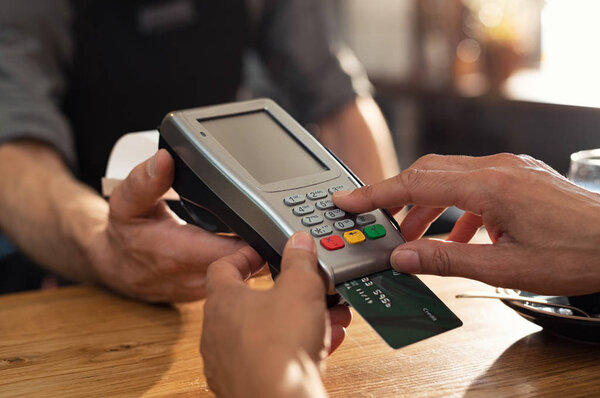 Closeup of hand using credit card swiping machine to pay. Female hand with credit card paying through terminal for payment in coffee shop. Woman entering debit card code in swipe machine.