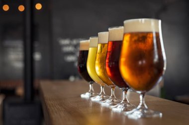 Gözlük ile zanaat bira ahşap çubuğu'nda farklı tür. Bira bira gözlük bir satırda düzenlenen dokunun. Beş bardak fıçı bira bir barda farklı türde closeup.