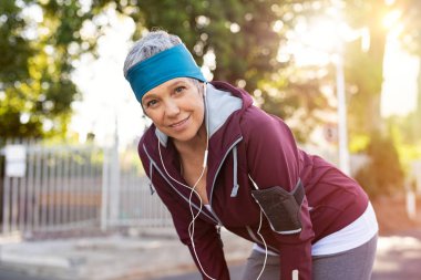 Üst düzey aktif kadın onun günlük rutin egzersiz tamamlanıyor. Günbatımı sırasında Park'ta jogging sonra dinlenme atletik Olgun kadın portresi. Yaşlı runner çalıştırdıktan sonra dinlenme sırasında müzik.