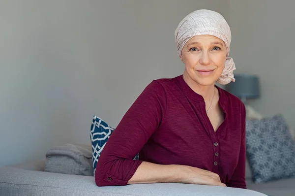 成熟的妇女与癌症的粉红色头巾微笑着坐在沙发上在家 接受化疗后坐着癌症的微笑的妇女 成熟女士肖像面对脱发 复制空间的副作用 — 图库照片