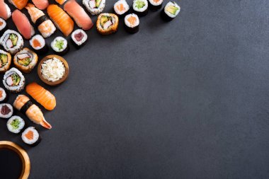 Top view of corner of hosomaki, uramaki, nigiri and soy sauce on blackboard. High angle view of fresh maki rolls and wooden bowl of rice on slate stone. Variety of sushi pieces on stone table with copy space. clipart