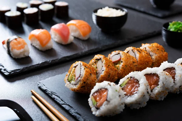 日本の寿司お食事をご飯と海苔を黒板の板 ロール寿司海老 アボカド クリーム チーズ Uramaki 食べロールパン 箸の黒いテーブルの上にぎり — ストック写真