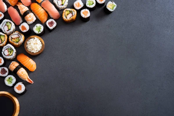 Hosomaki Uramaki 握和酱油在黑板上的角落的顶部视图 在石板石上的新鲜的 Maki 卷和木碗大米的高角度视图 复制空间石桌上的各种寿司片 — 图库照片