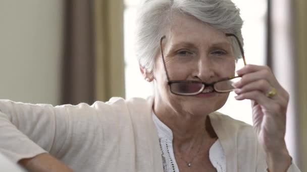 愉快的退休老年妇女看着相机 而持有眼镜 微笑满意的妇女在家里戴眼镜 特写脸的老祖母尝试新的眼镜 带眼镜的美丽的老年妇女在家微笑 — 图库视频影像