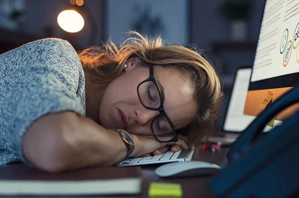 成熟したビジネス女性着て眼鏡と オフィスのコンピューターのキーボード上で眠っています 残業寝てやって疲れて実業家の顔をクローズ アップ 暗いオフィスで眠そうなブロンドの女性の肖像画 過労と先延ばしのコンセプト — ストック写真