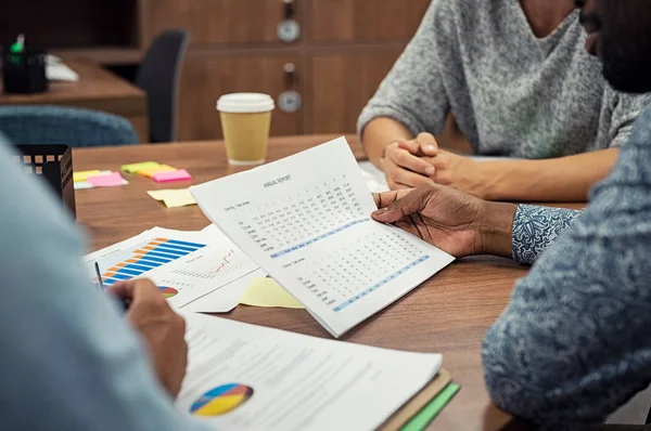 Closeup of business man hands reading annual report with his colleagues during a meeting. African businessman checking past sales report for merger at office. Hands holding document in a boardroom.