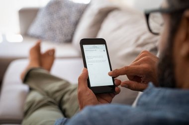 İnternet tarayıcısı ile cep telefonu ekran üzerinde tutan bir adam el closeup. Cep telefonu bakarken kanepede oturan dinlendirici gözlük olan adam. Olgun latin erkek evde e-posta kontrol için smartphone kullanarak closeup.