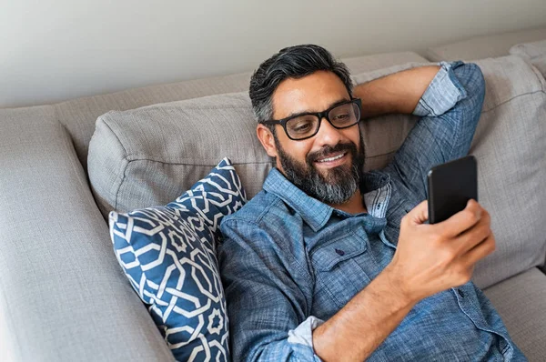 Homem Latino Sorridente Feliz Usando Dispositivo Smartphone Enquanto Sentado Sofá — Fotografia de Stock