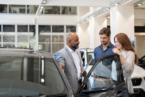 Couple examining new auto with car dealer — Stock Photo, Image