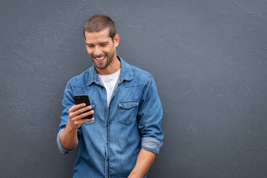 Gri duvarda akıllı telefon kullanan serin gülümseyen adam