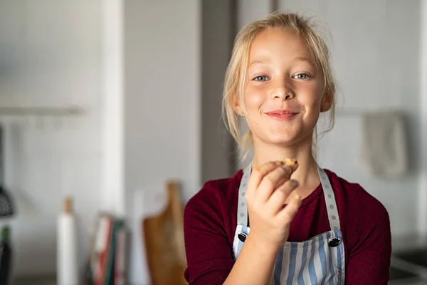 Menina engraçada no avental comer biscoito artesanal — Fotografia de Stock