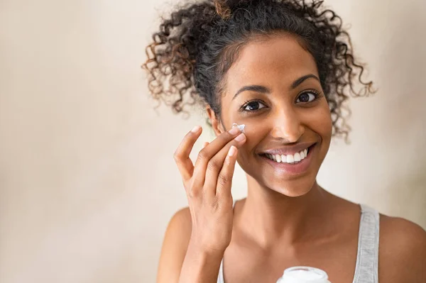 Menina bonita aplicando creme facial — Fotografia de Stock