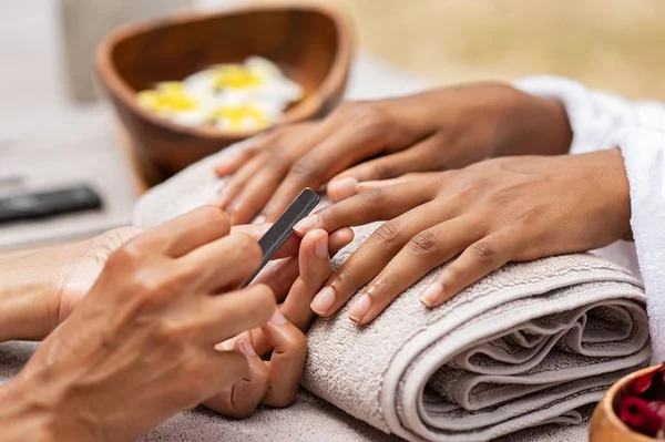 Beautician file nails to a black hand — Stock Photo, Image