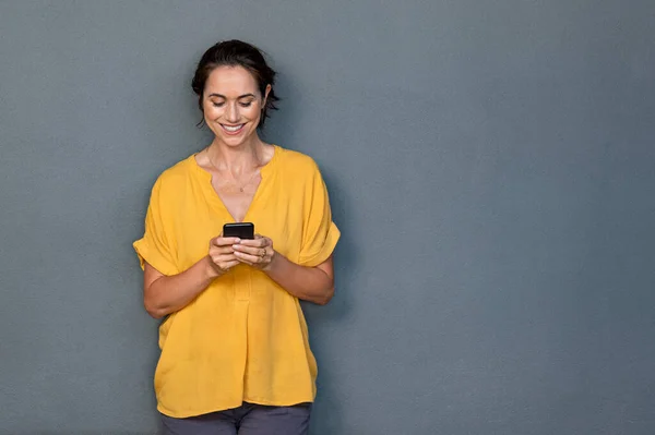 Mulher latina madura usando telefone inteligente na parede cinza — Fotografia de Stock