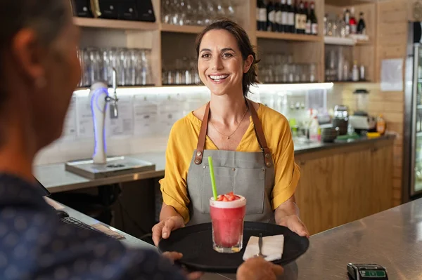 Smiling waitress serving strawberry smoothie
